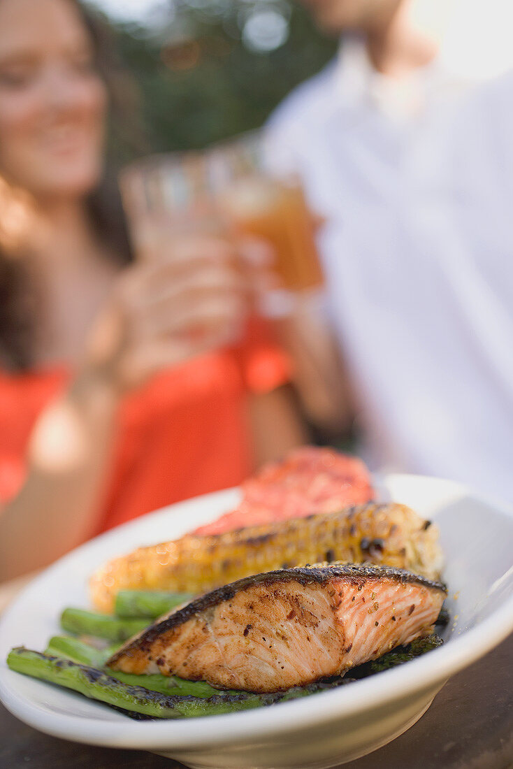 Grilled salmon with accompaniments, couple clinking glasses