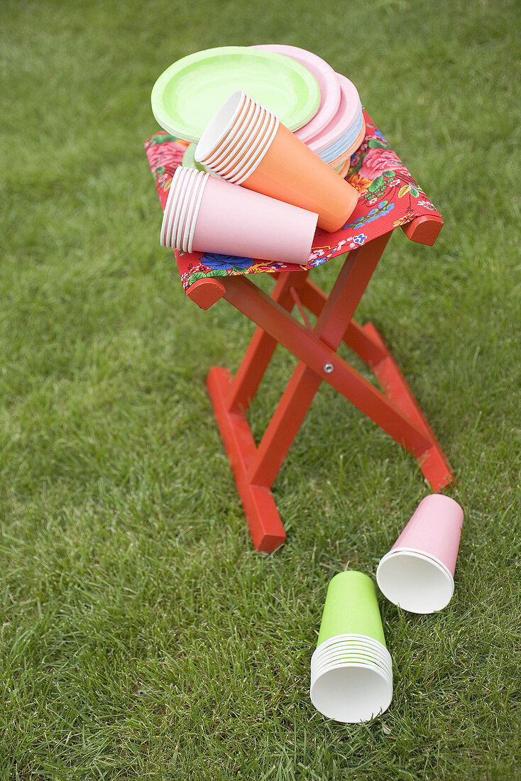 Coloured paper cups and plates on folding stool in garden
