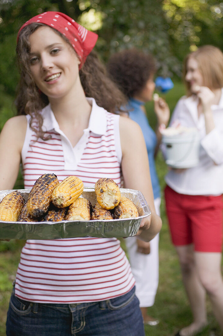 Junge Frau serviert gegrillte Maiskolben beim Grillfest