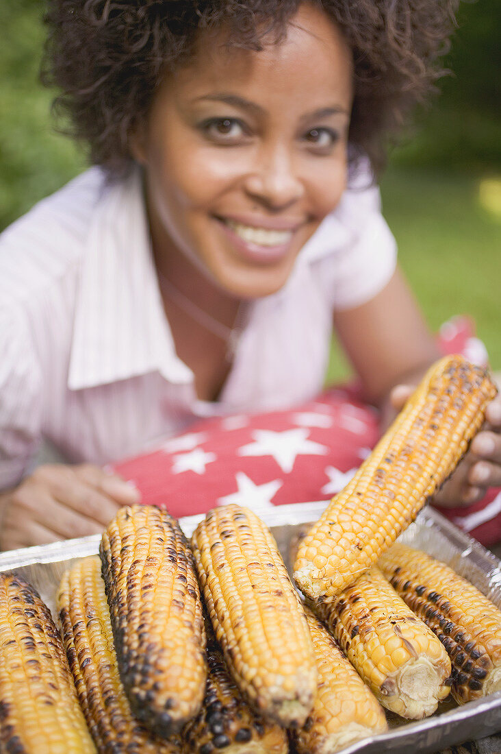 Woman taking grilled corn on the cob out of aluminium dish