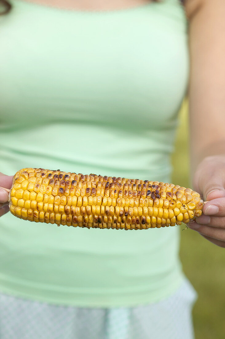 Frau hält gegrillten Maiskolben