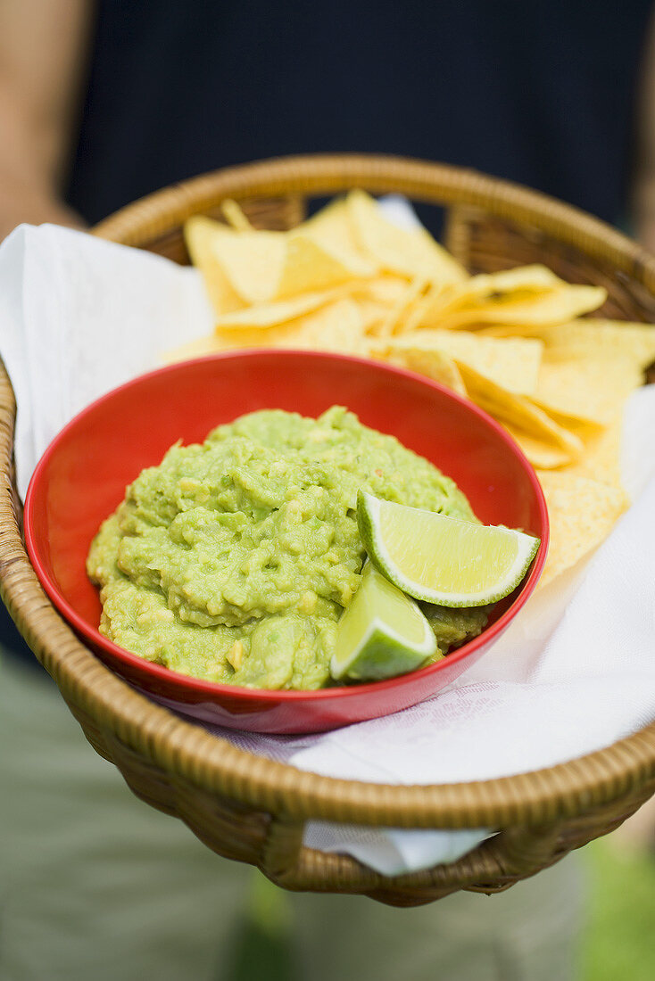 Person holding basket of guacamole and tortilla chips