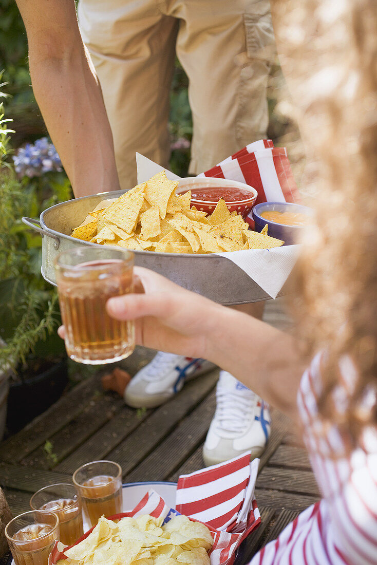 Man holding tray of tortilla chips & dips, woman with iced tea