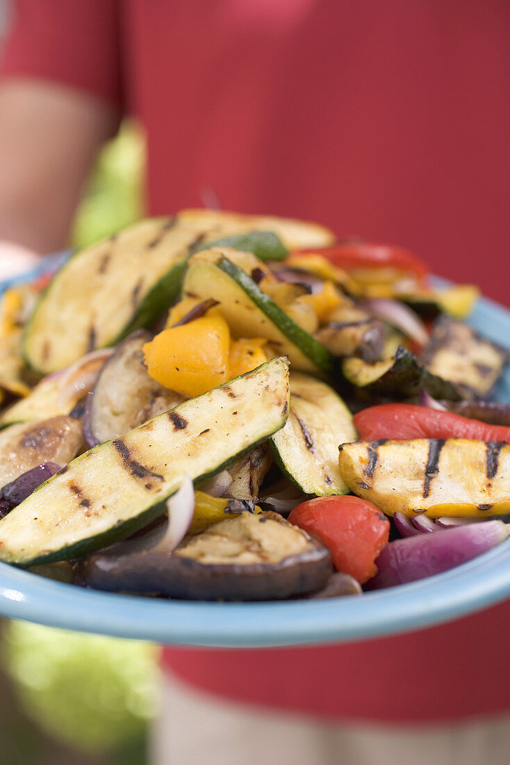 Person holding a plate of grilled vegetables