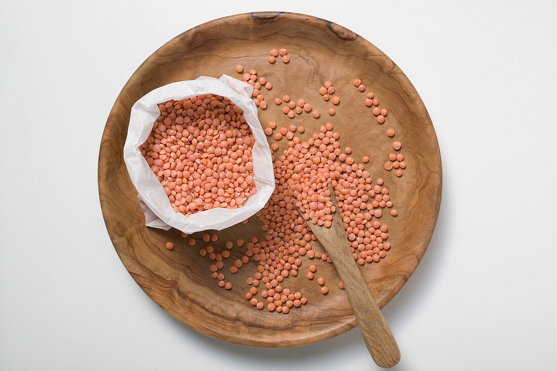 Red lentils on wooden plate and in bag