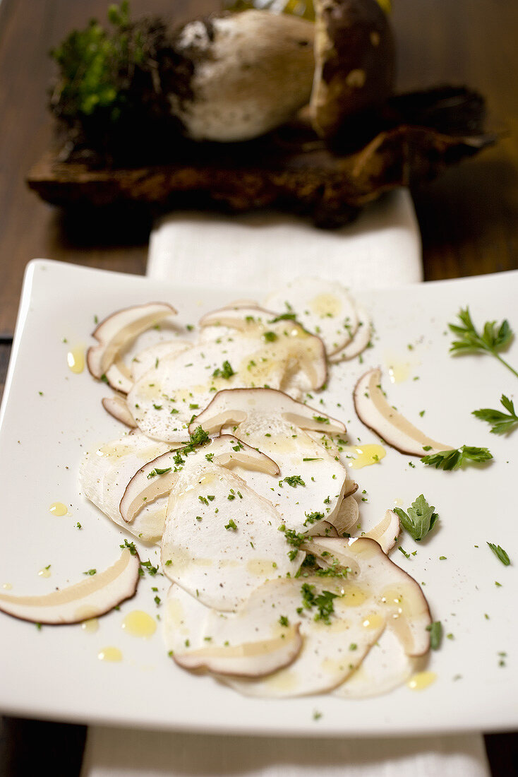 Steinpilzcarpaccio auf Schneidebrett vor frischem Steinpilz