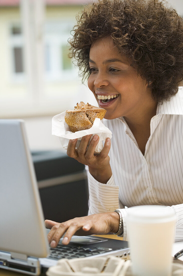 Woman eating muffin while working on computer