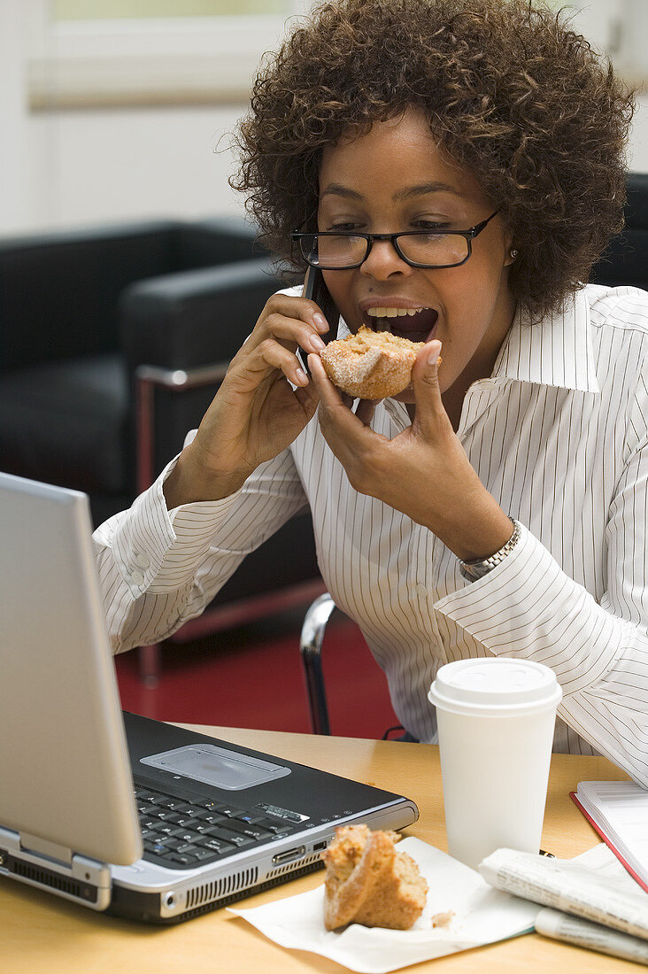 Woman eating muffin while working on computer