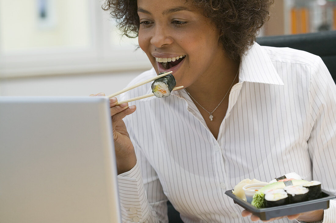 Frau isst Sushi im Büro