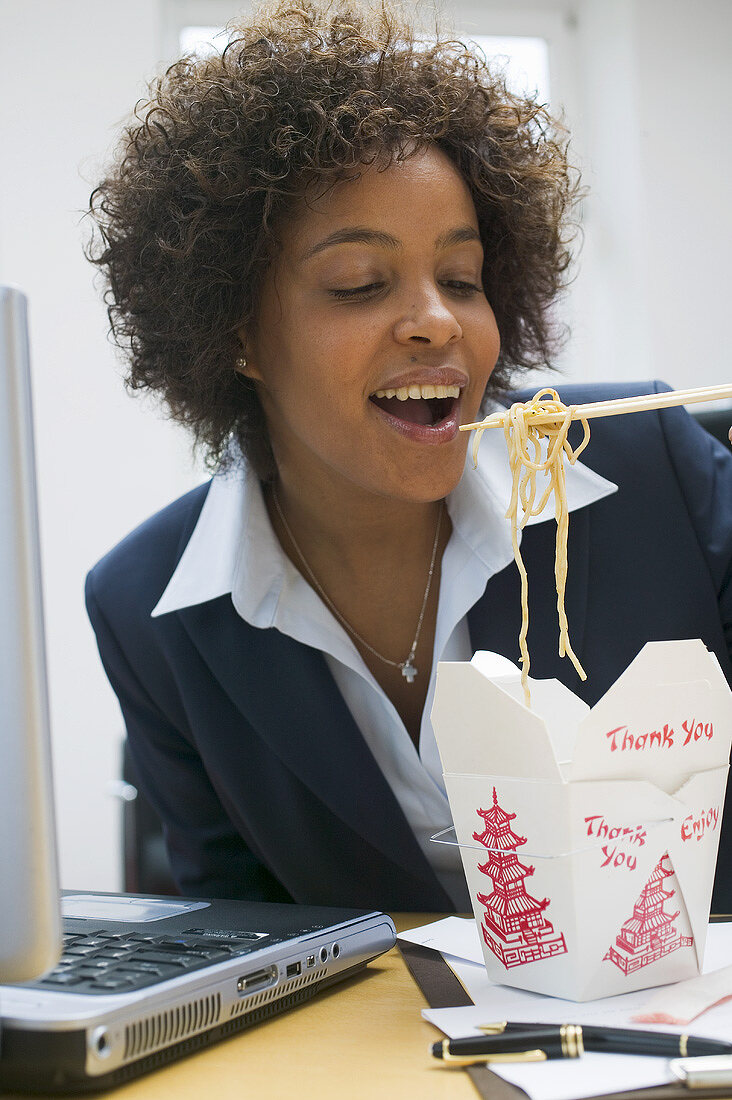 Woman in office eating Asian noodle dish