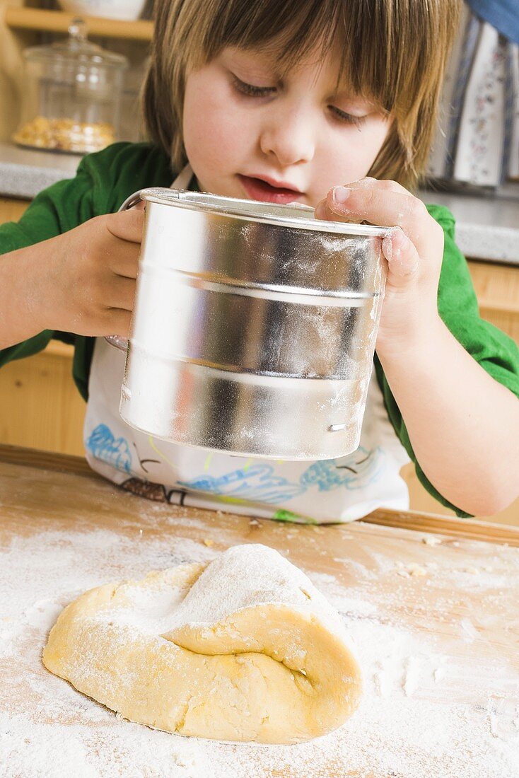 Child sifting flour onto dough