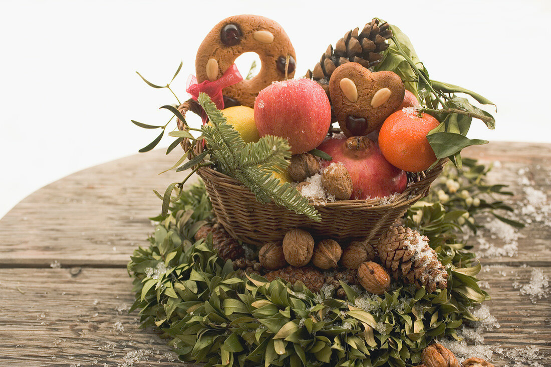 Lebkuchen mit Obst, Nüssen, Zapfen im Korb auf Buchsbaumkranz