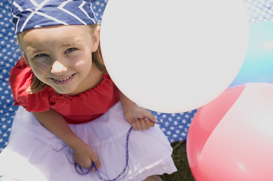 Small girl holding balloons in garden on the 4th of July