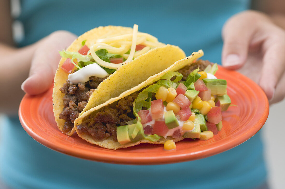 Woman holding two tacos on a plate