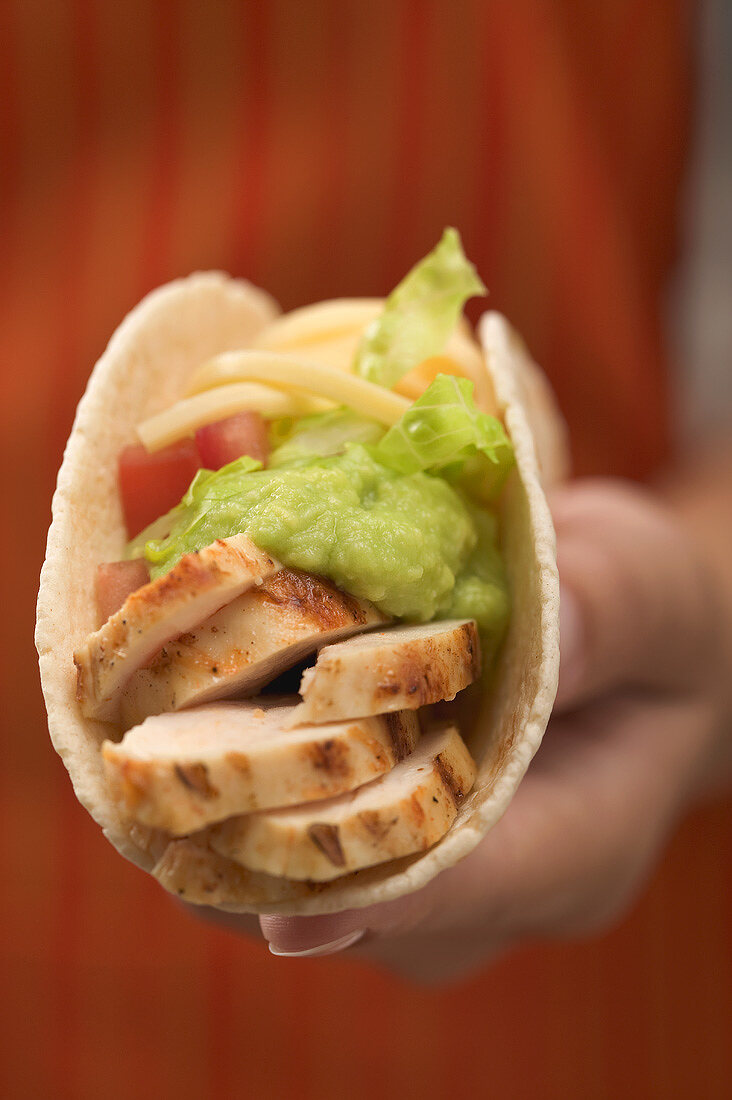 Hand hält Taco mit Hähnchen und Guacamole