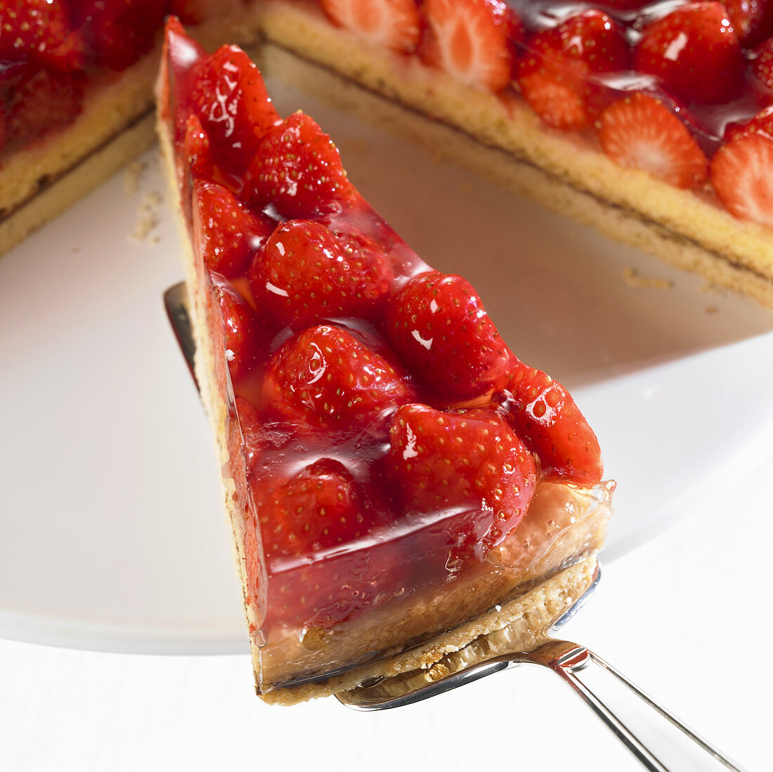 Stück Erdbeertorte auf Heber vor angeschnittener Torte