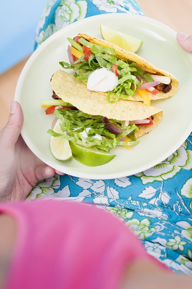 Frau hält Teller mit zwei Tacos