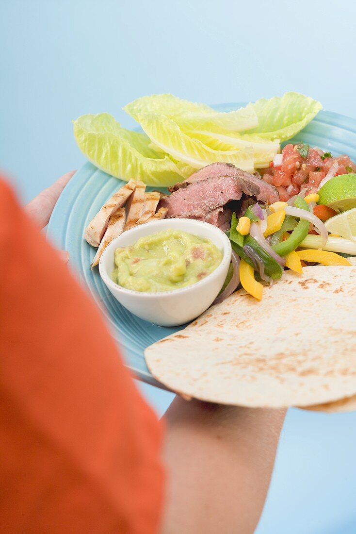 Person holding fajita and guacamole on plate