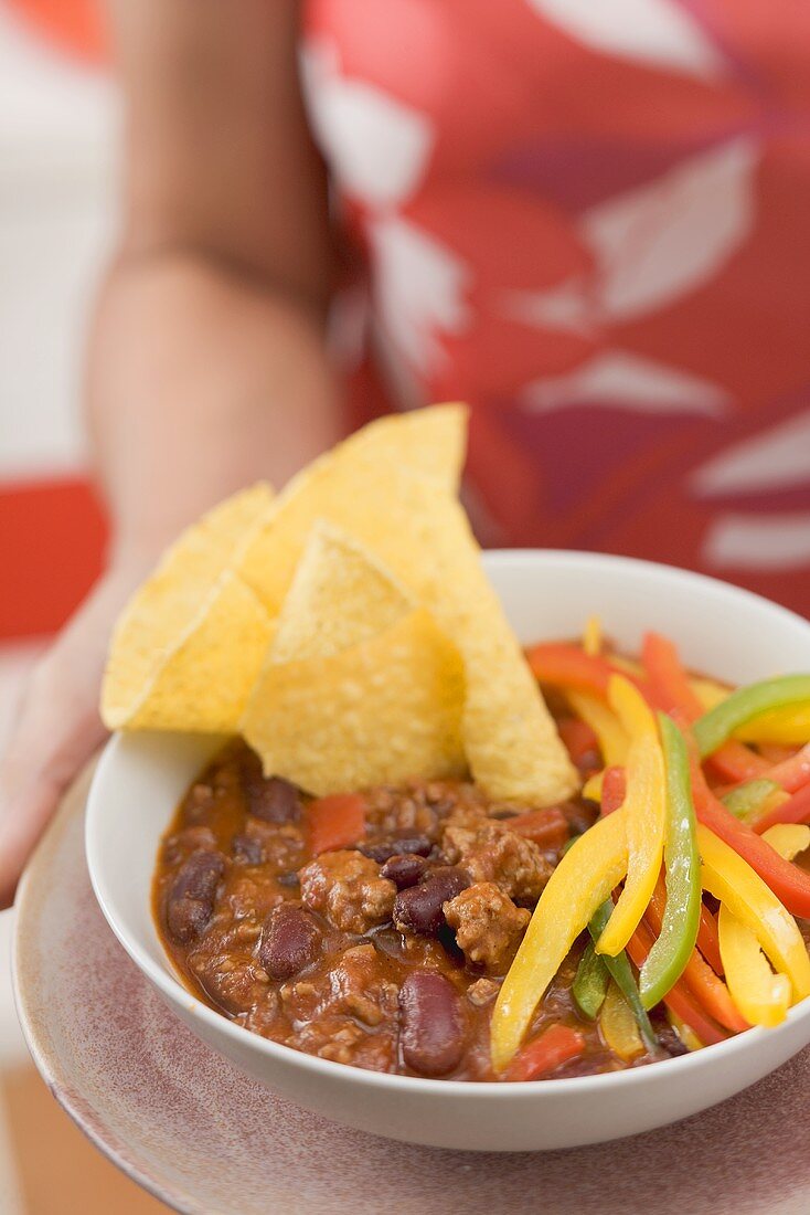 Frau serviert Chili con Carne mit Nachos und Paprika