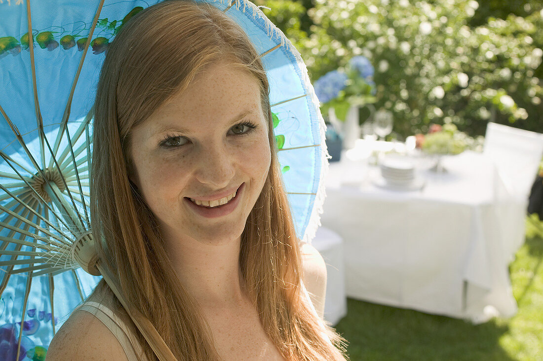 Frau mit Sonnenschirm vor gedecktem Tisch im Freien