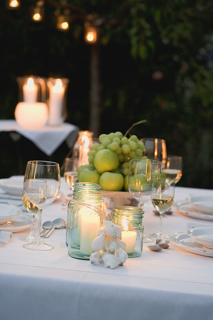 Bowl of fruit and windlights on table laid in garden