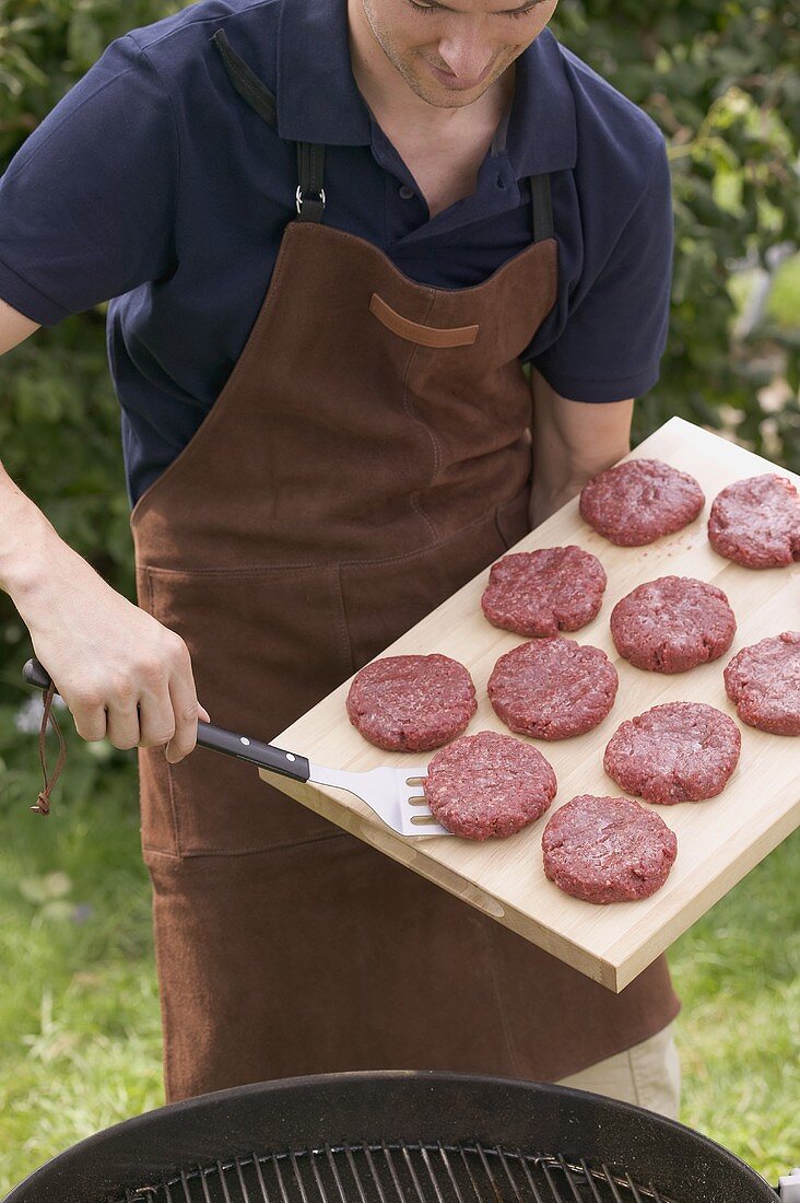 Man lifting raw burgers from chopping board on to barbecue