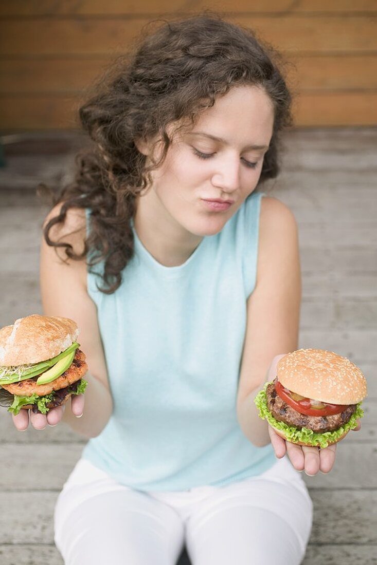 Frau hält unentschlossen zwei verschiedene Burger