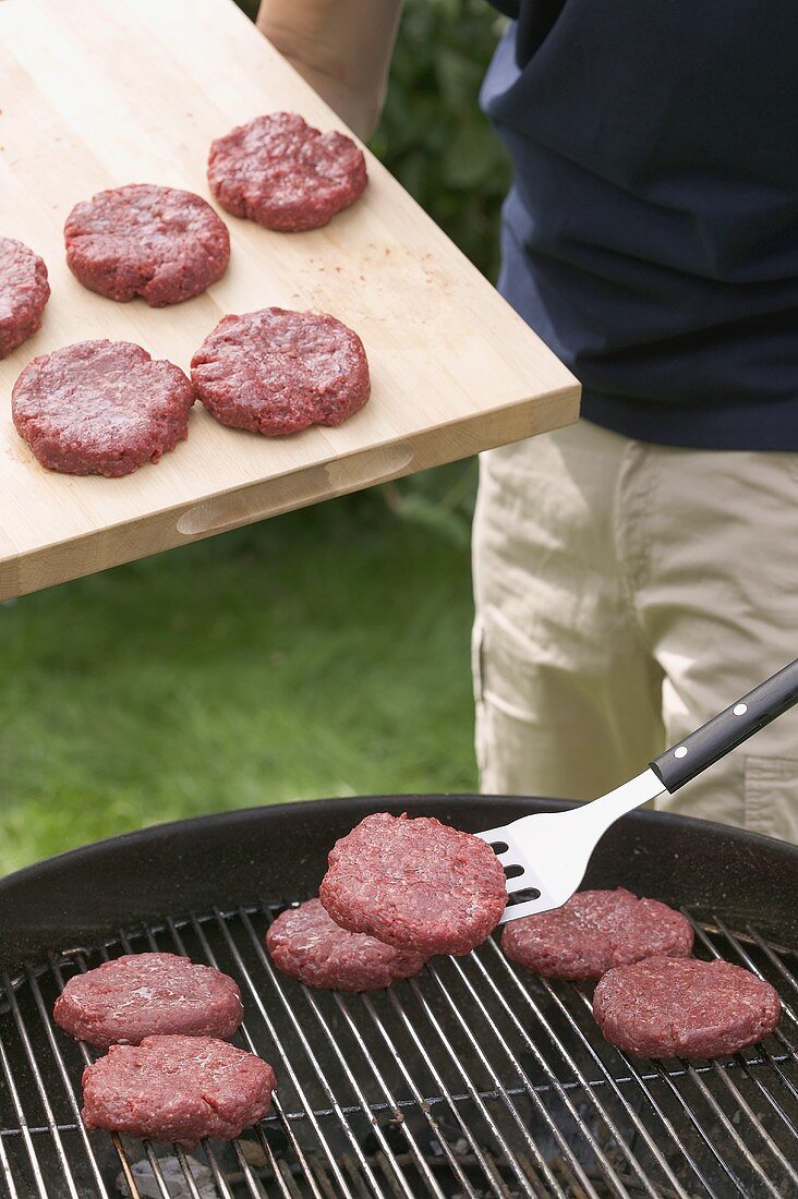 Mann legt rohe Frikadellen auf den Grillrost