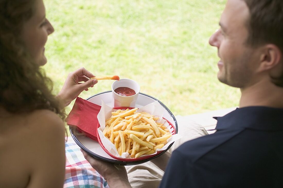 Paar isst Pommes frites mit Ketchup im Garten