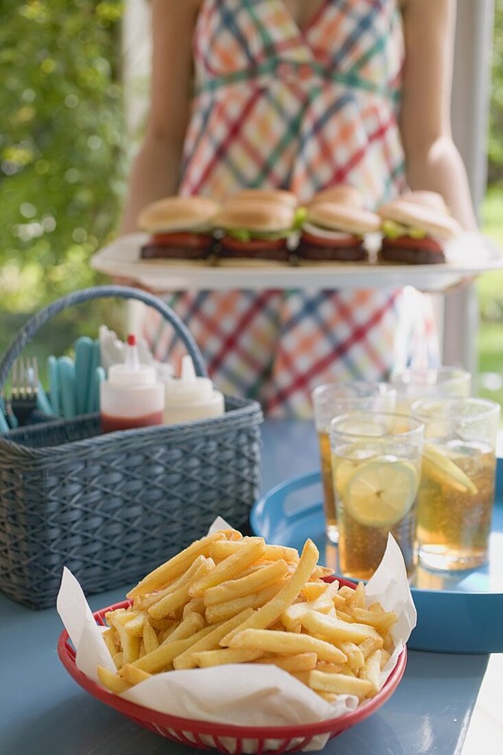 Pommes frites und Eistee auf Tisch, Frau serviert Hamburger