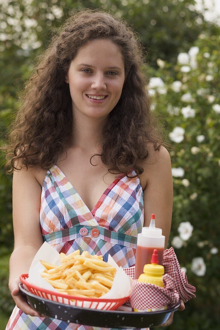 Frau hält Tablett mit Pommes frites, Ketchup und Senf