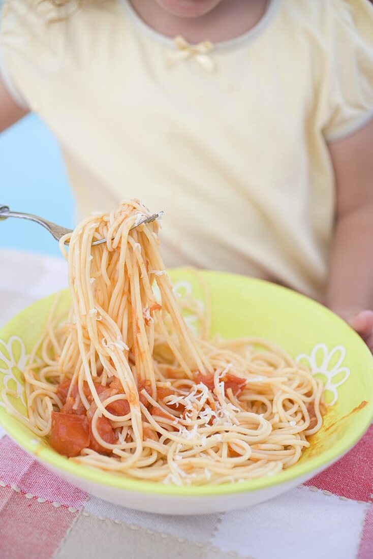 Small girl eating spaghetti with tomato sauce and Parmesan