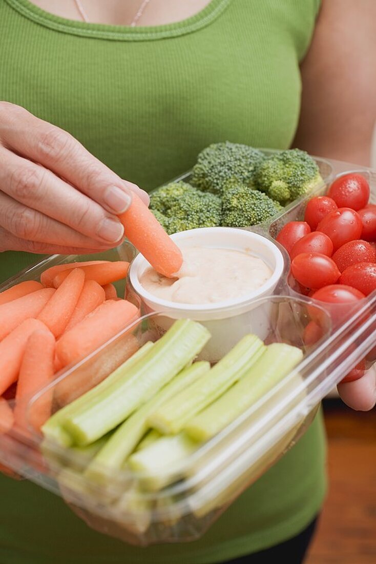 Frau hält Plastikschale mit Gemüse und Dip