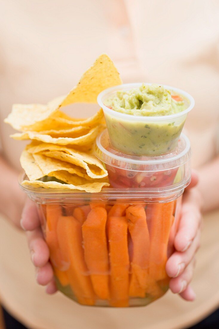Woman holding plastic containers of vegetables & dips & nachos