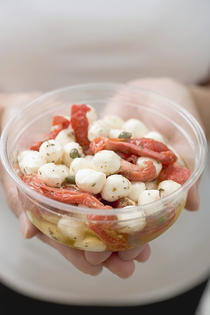 Woman holding plastic container of mozzarella and tomatoes