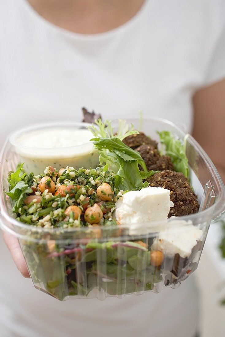 Frau hält Plastikschale mit Salat, Feta und Dressing