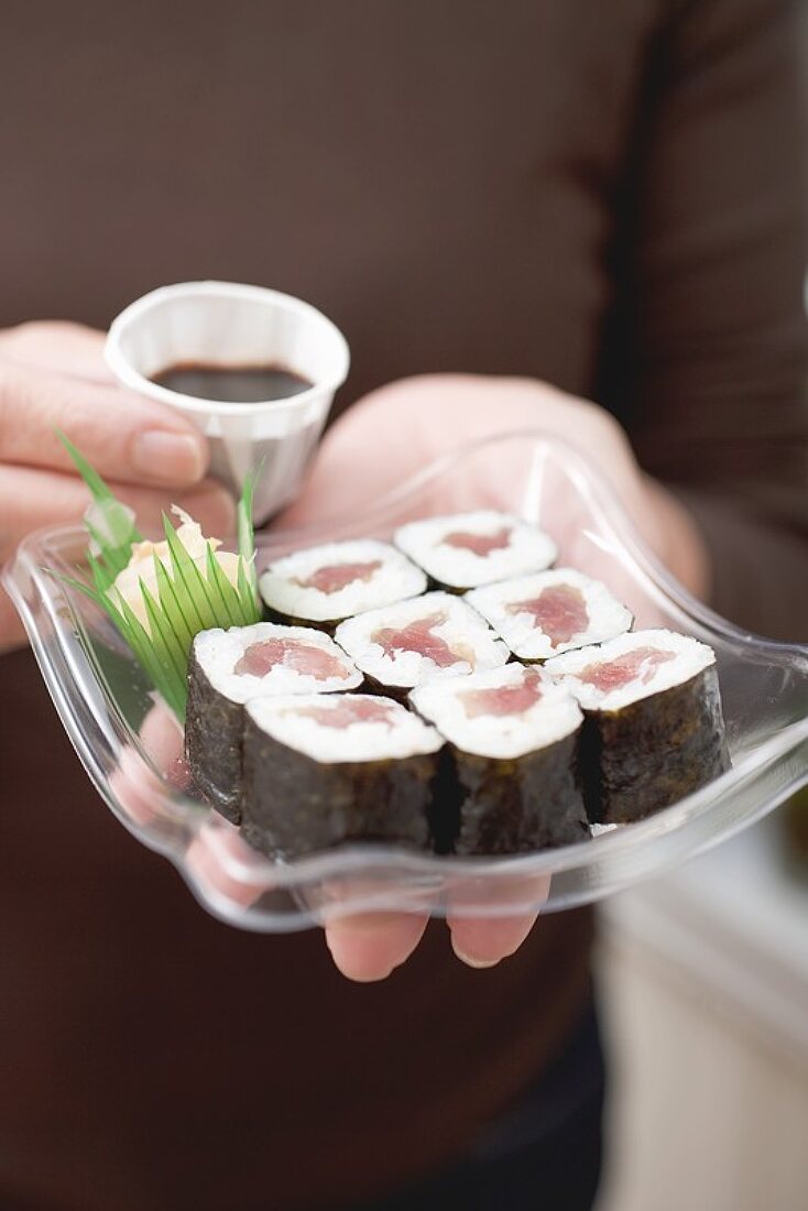 Frau hält Plastikschale mit Maki-Sushi und Sojasauce