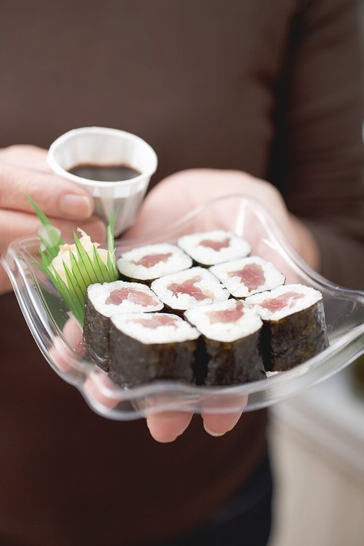 Woman holding maki sushi and soy sauce on plastic tray