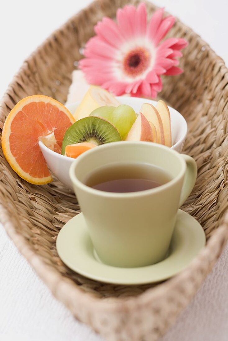 Teetasse, frische Früchte, Handtuch und Blume im Korb