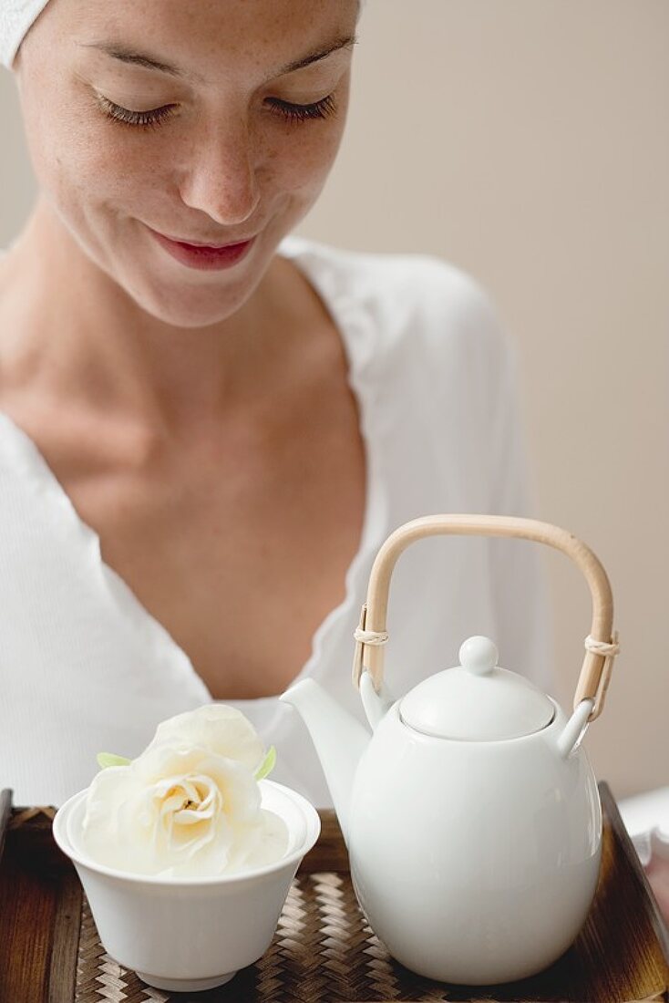 Frau hält Tablett mit Tee und weisser Blüte