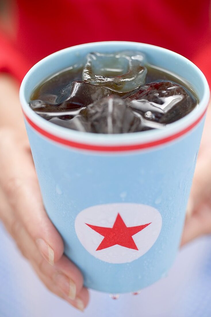 Woman holding beaker of cola with ice cubes