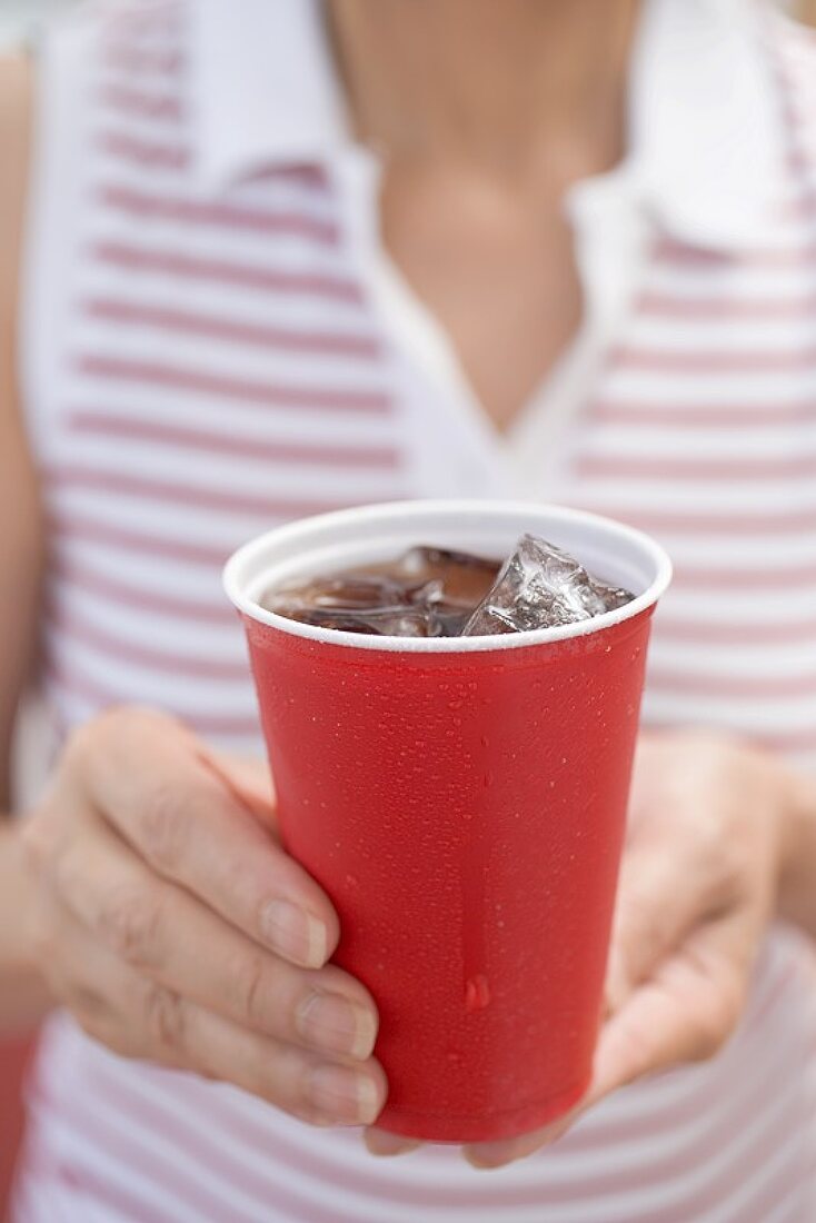 Woman holding beaker of cola with ice cubes