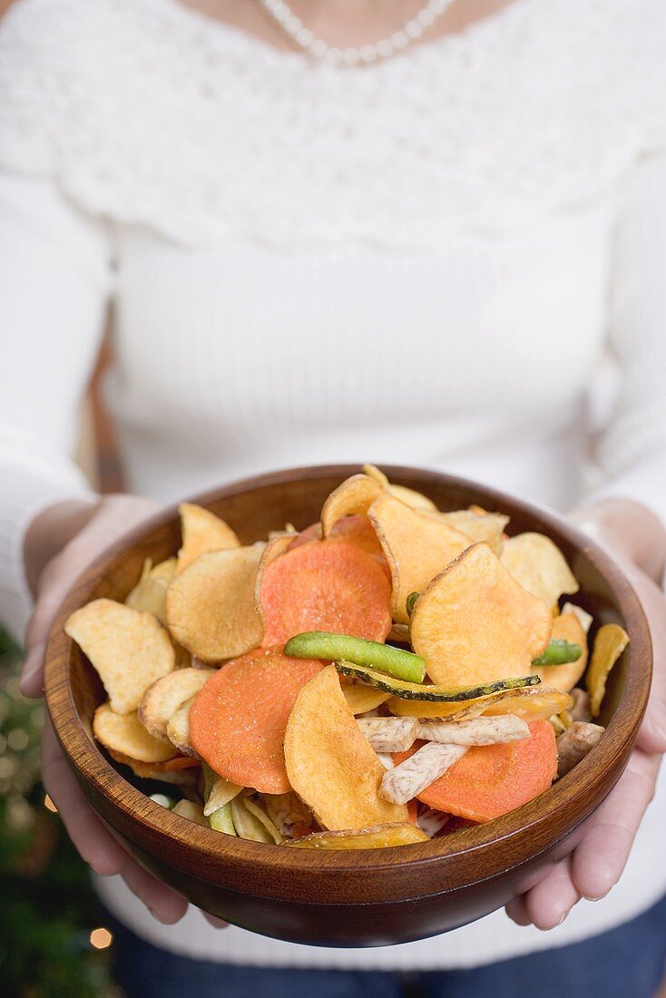 Woman holding wooden bowl of vegetable crisps