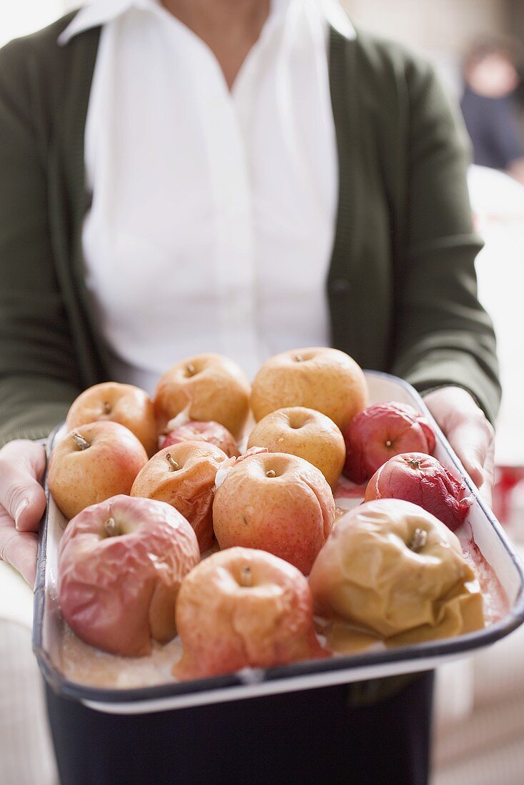 Woman holding baked apples on baking tray