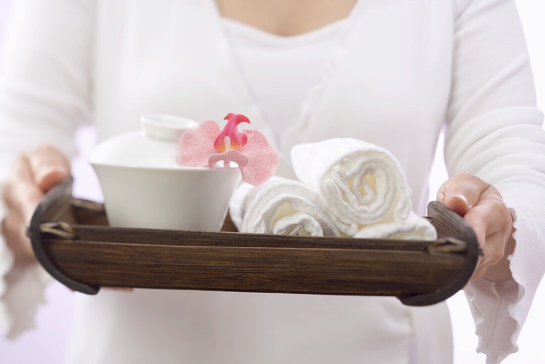 Frau hält Tablett mit Handtüchern, Schale und Orchidee