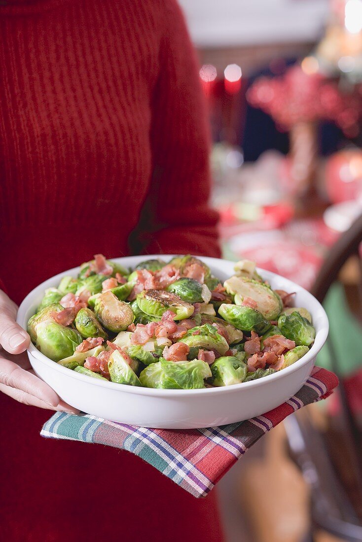 Frau hält Schüssel Rosenkohl mit Speck (weihnachtlich)