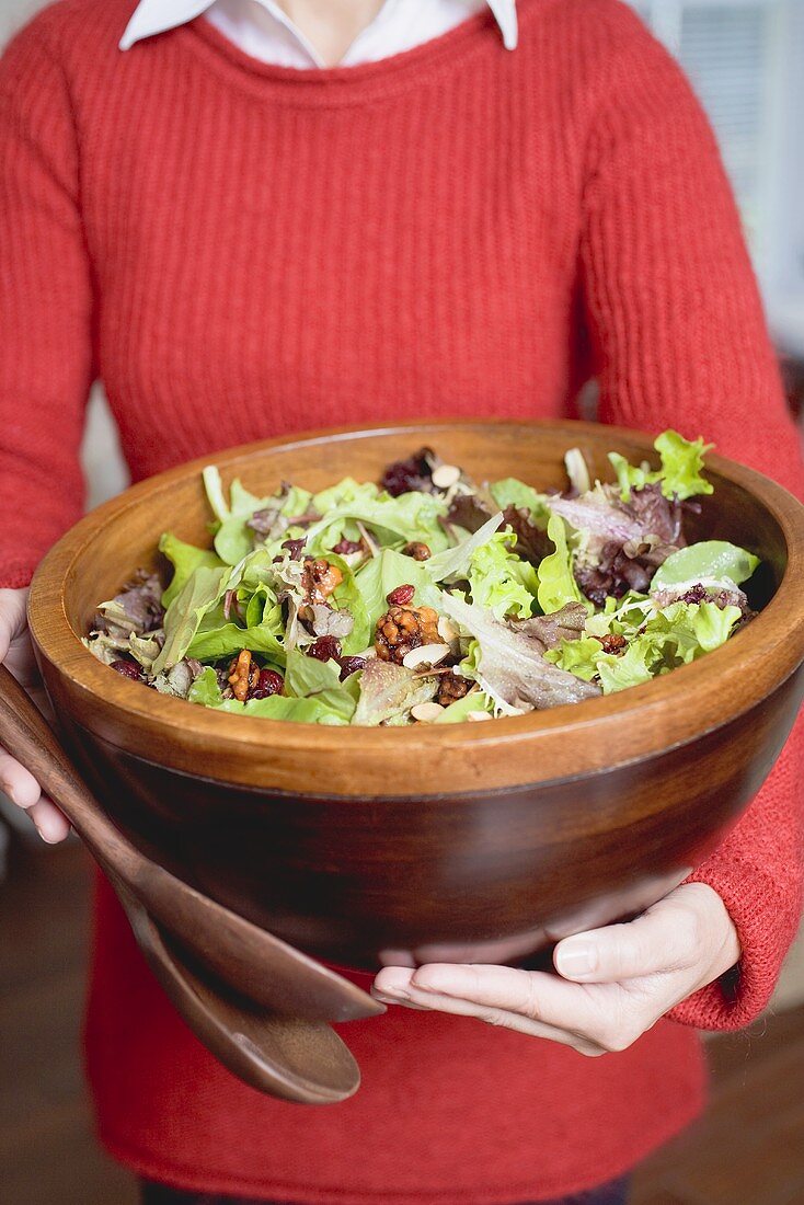 Woman holding large bowl of salad leaves with nuts