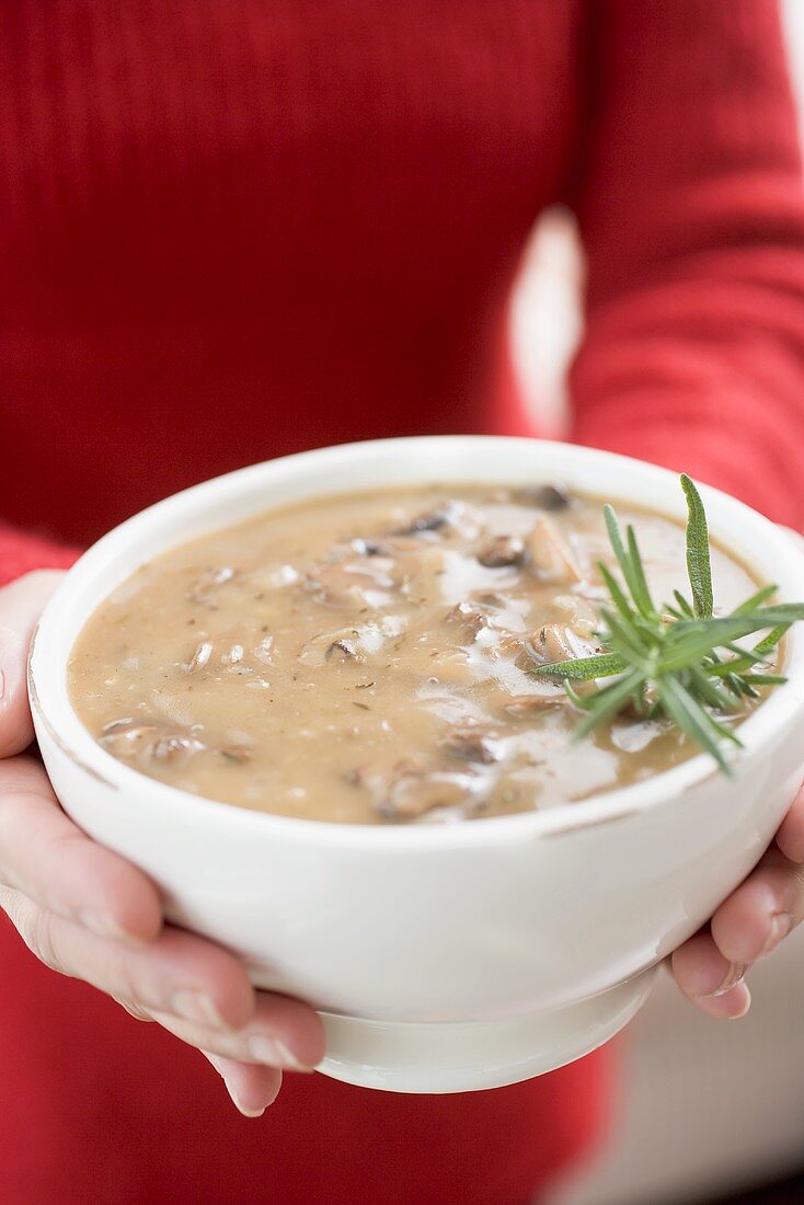 Frau hält Schale Champignonsauce mit Rosmarin