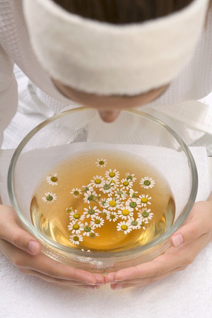 Woman bending over bowl of chamomile tea with flowers