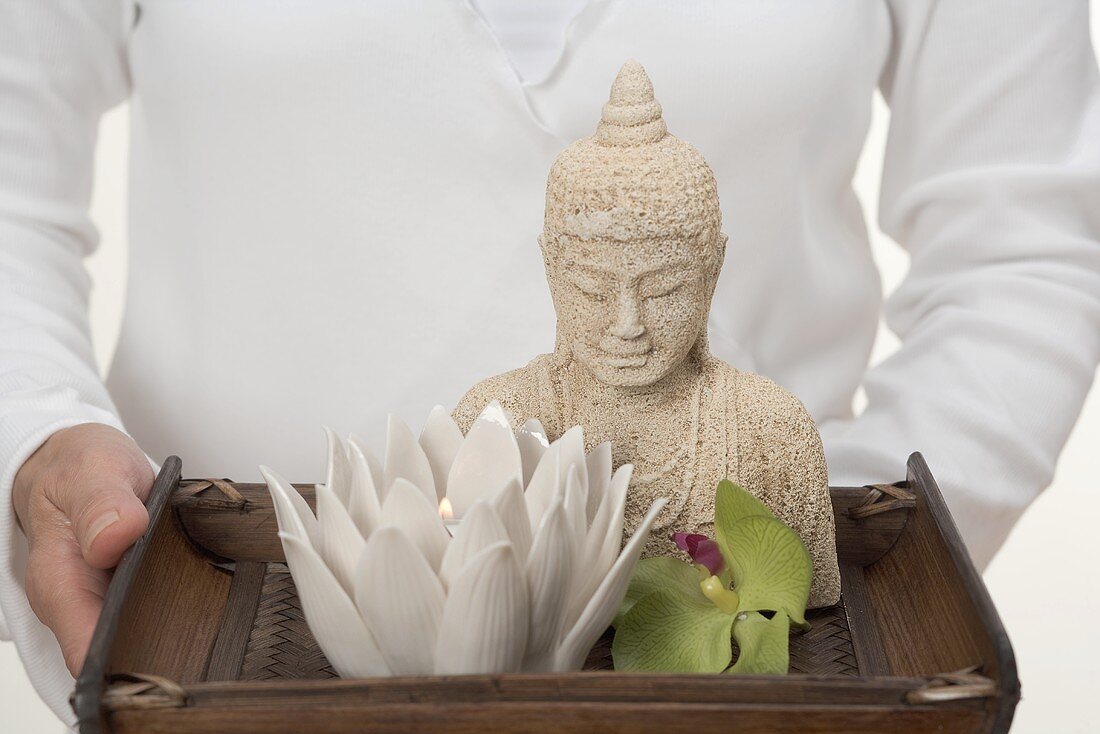 Woman holding Buddha statue, candle and orchid on tray